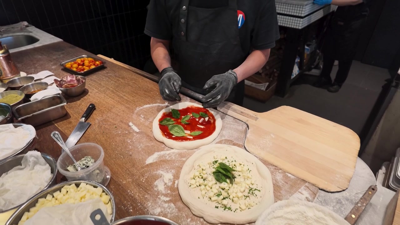 Inquadratura dall'alto di uno chef che guarnisce impasto per pizza fatto a mano con basilico fresco e salsa di pomodoro.