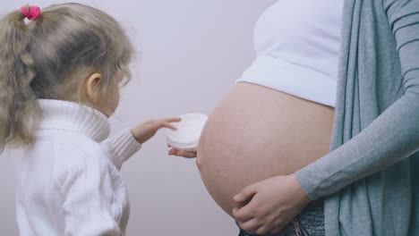 girl with ponytail applies cream on pregnant mother tummy