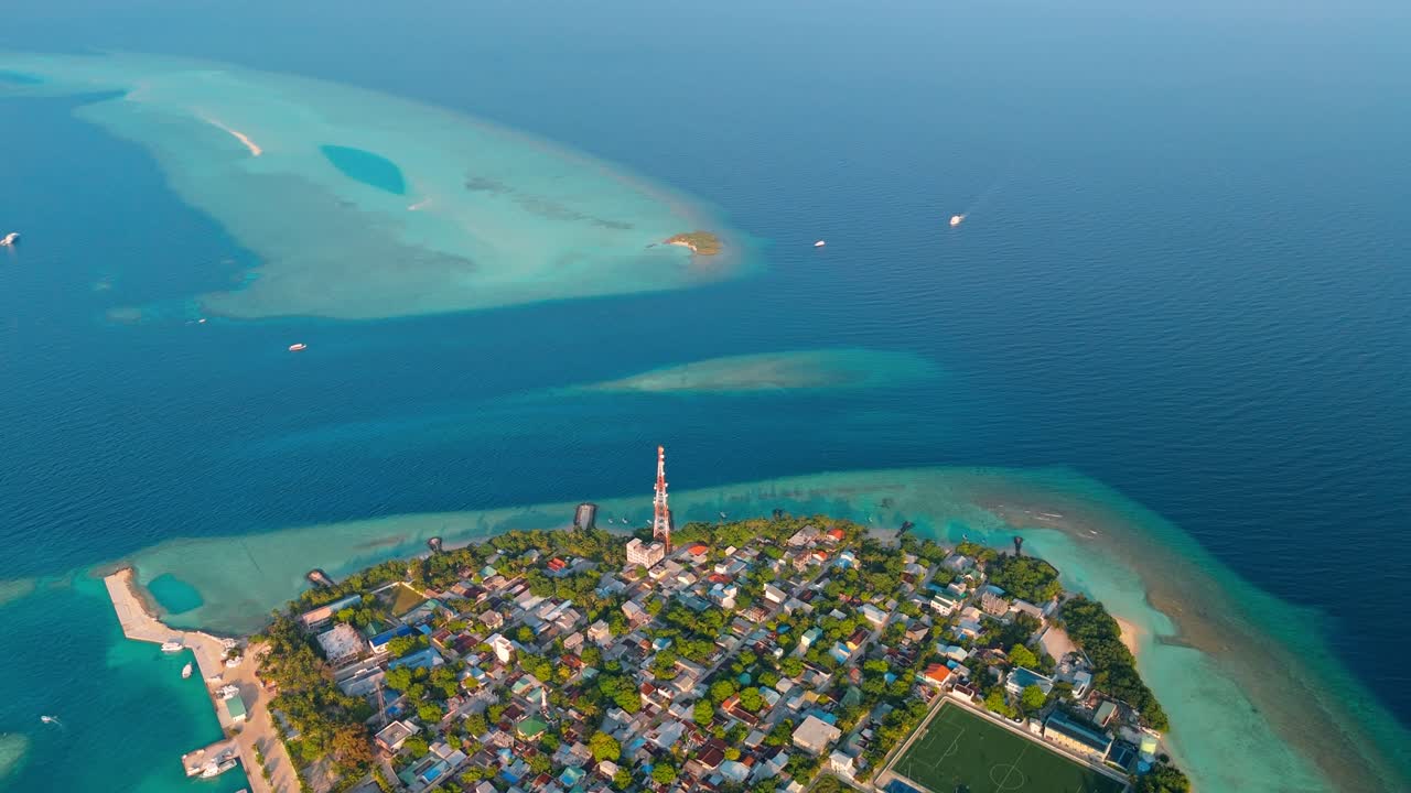 A stunning aerial drone view showcasing Rasdhoo Island surrounded by crystal-clear turquoise waters and vibrant coral reefs in the Maldives.