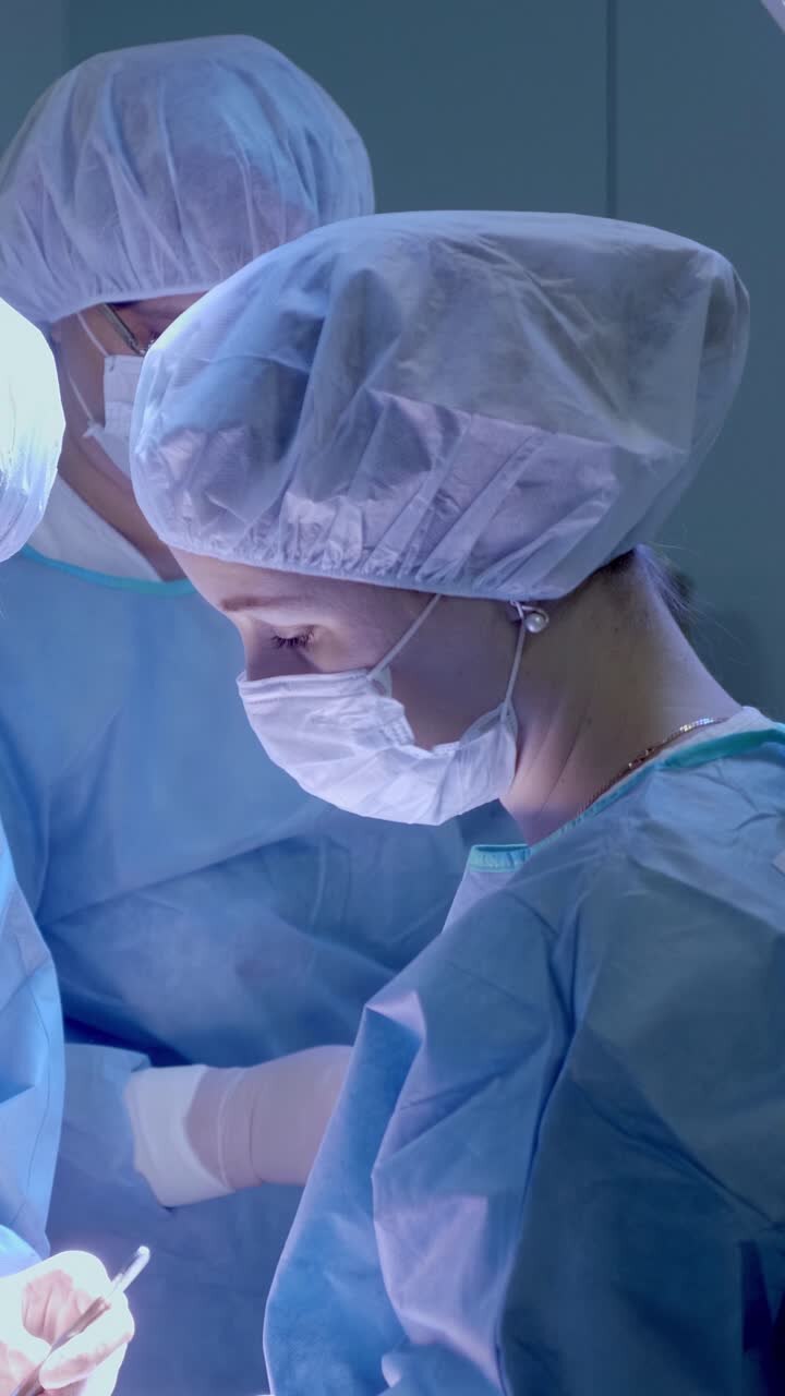 Medical team in blue scrubs performing surgery with focused expressions and bright lighting