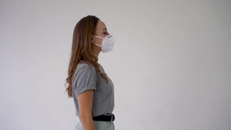 young woman takes off medical face mask and takes a deep breath smiling. end of the covid-19 quarantine. copy space and white background. confident female looking at camera. side view.