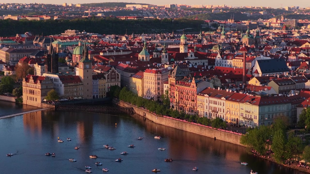 Veduta aerea con drone del fiume Moldava con pedalò, l'argine della città vecchia di Praga con una torre dell'orologio e facciate storiche che risplendono nella calda luce del tramonto, Praga, Repubblica Ceca.