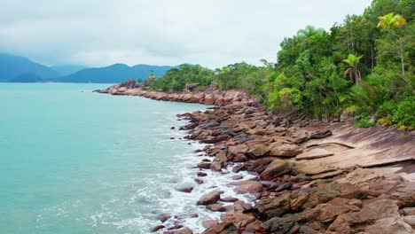 proximity aerial shot of rocky coast with crashing waves and green vegetation during a cloudy and cosy day