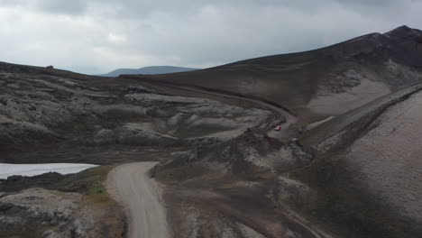 Drone-View-Coche-Conduciendo-Por-Un-Camino-De-Tierra-En-Un-Paisaje-Desértico-Rocoso-En-Islandia.-Exploración-Y-Aventura.-Ojo-De-Pájaro-Del-Camino-Sinuoso-Y-El-Paisaje-Surrealista-De-Las-Tierras-Altas-Islandesas
