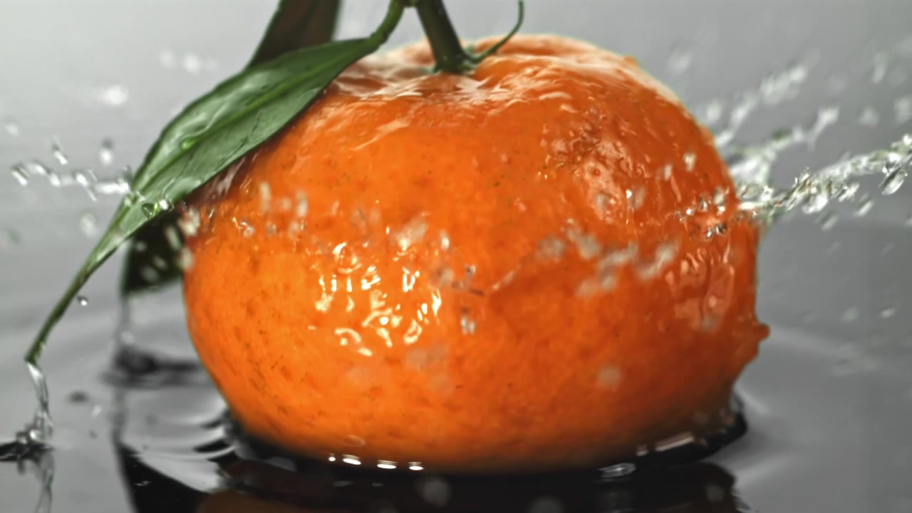 Mandarino fresco con foglia verde che si tuffa nell'acqua al rallentatore