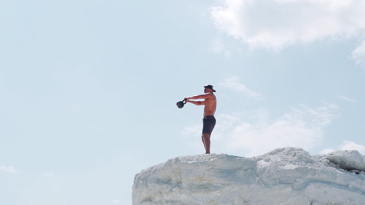 Shirtless male athlete doing exercises with kettlebell. Outdoor training. Slow motion