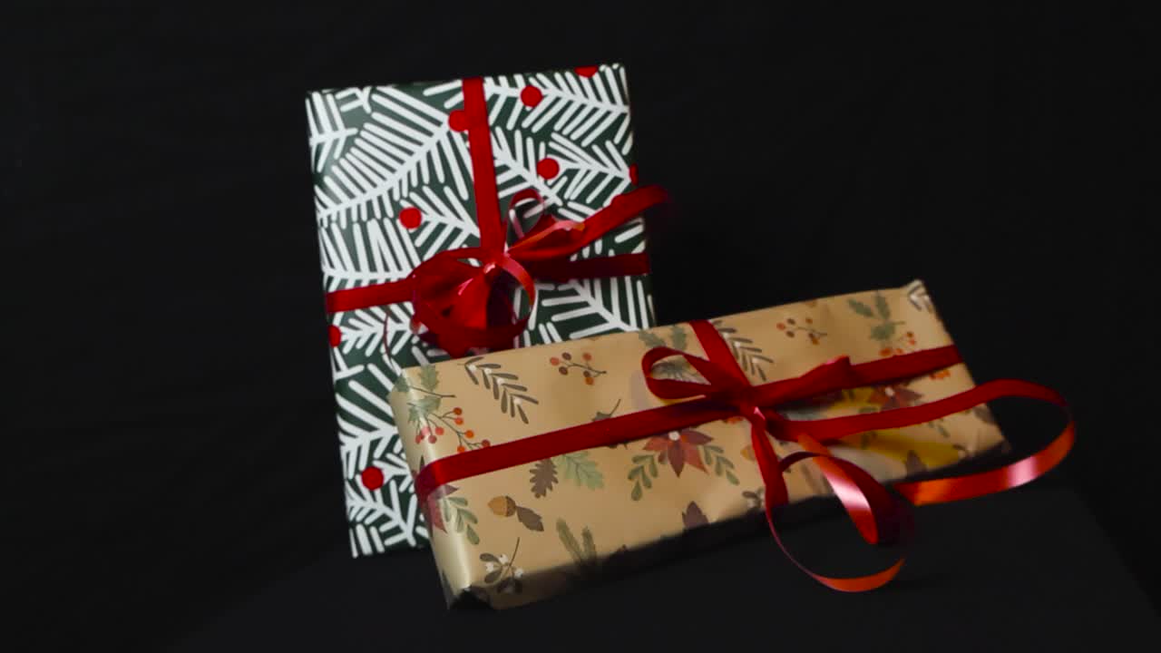 близкие кадры, которые медленно вращаются от рождественских подарков и подарков с праздничной упаковкой бумаги и красными лентами на черном темном фоне. подарки находятся под хорошим освещением, делая тени