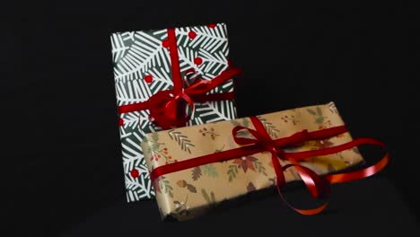 close up footage that is spinning around slowly from christmas presents and gifts with holiday wrapping paper and red ribbons on a black dark background. presents are under good lights, making shadows