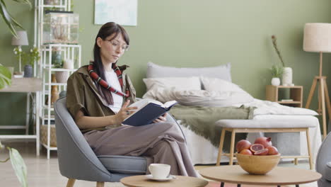 Mujer-Joven-Con-Su-Mascota-Serpiente-Alrededor-Del-Cuello-Leyendo-Un-Libro-Mientras-Se-Sienta-En-Un-Sillón-En-Casa