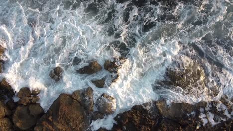 Rising-bird's-eye-view-looking-down-on-waves-crashing-on-a-rocky-shore