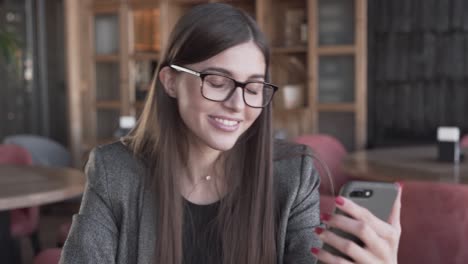 jovencita bonita con una sonrisa hermosa sentada en un café acogedor y hablando en su teléfono inteligente
