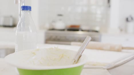 Mixing-bowl-of-cake-mix,-bottle-of-milk-and-rolling-pin-on-counter-top-in-kitchen,-with-copy-space