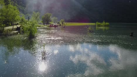 fly over a beautiful lake sun reflects on shallow surface of lake water plants around and a family enjoy outdoor weekend boat sailing picnic barbeque in forest azerbaijan and wood fire smoke visible