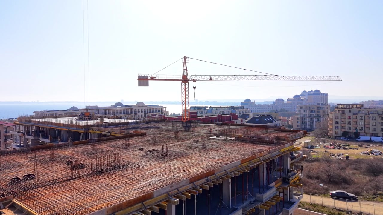 Construction site with crane, Bulgaria. Elevated perspective of building framework, metal reinforcement bars, and yellow tower crane under clear sky.