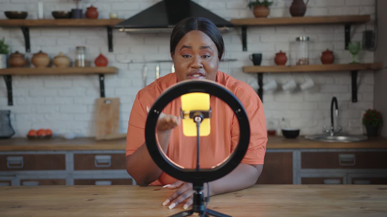 Plump blogger with ponytail speaks at tripod with smartphone