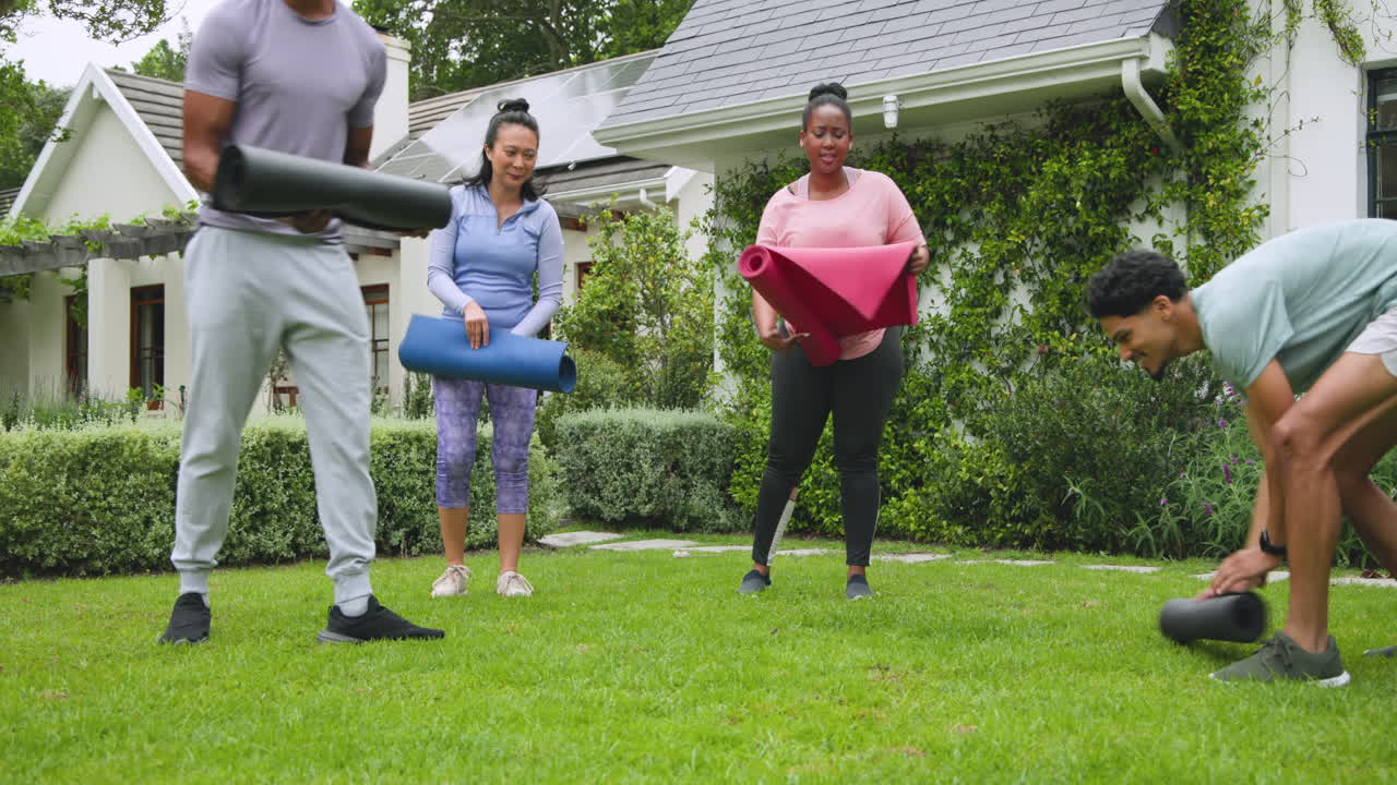 diverse friends setting up yoga mats on grass for outdoor exercise session