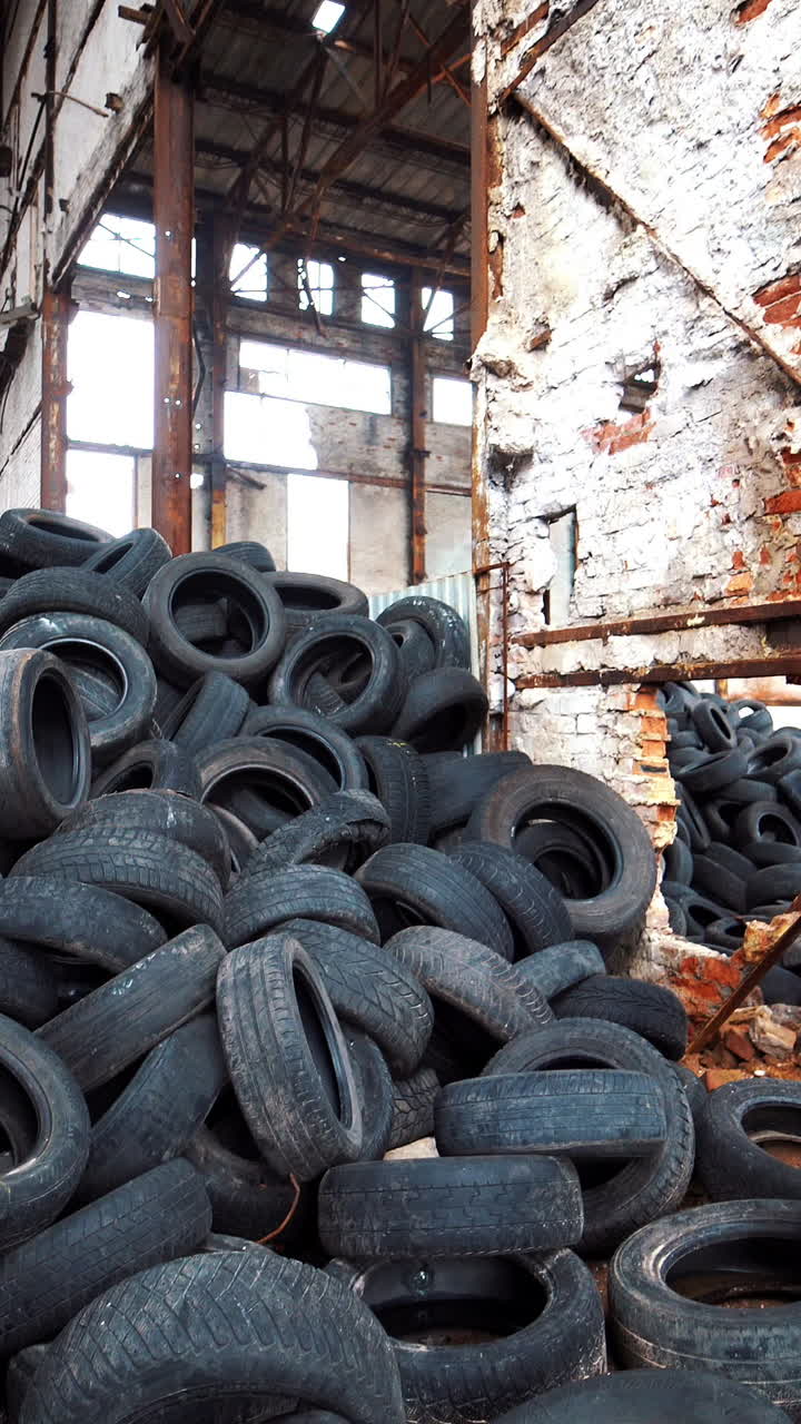 Old broken-down building inside with many tires on a large bunch. Black used rubber tires of vehicles on a desolate plant Vertical video