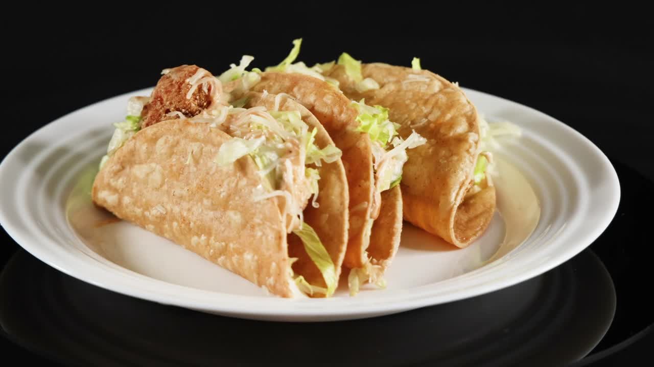 Tre tacoskaller fyldt med kød og salat roterer langsomt på en hvid tallerken.