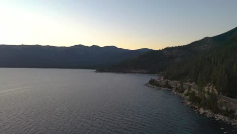 Wunderschönes-Alpenglühen-In-Den-Bergen-Des-Lake-Taho-über-Unberührten-Ruhigen-Wassern-Und-Einem-Kiefernwald-In-Kalifornien-Bei-Sonnenuntergang---Luftdrohne-Schwenkt-Nach-Links