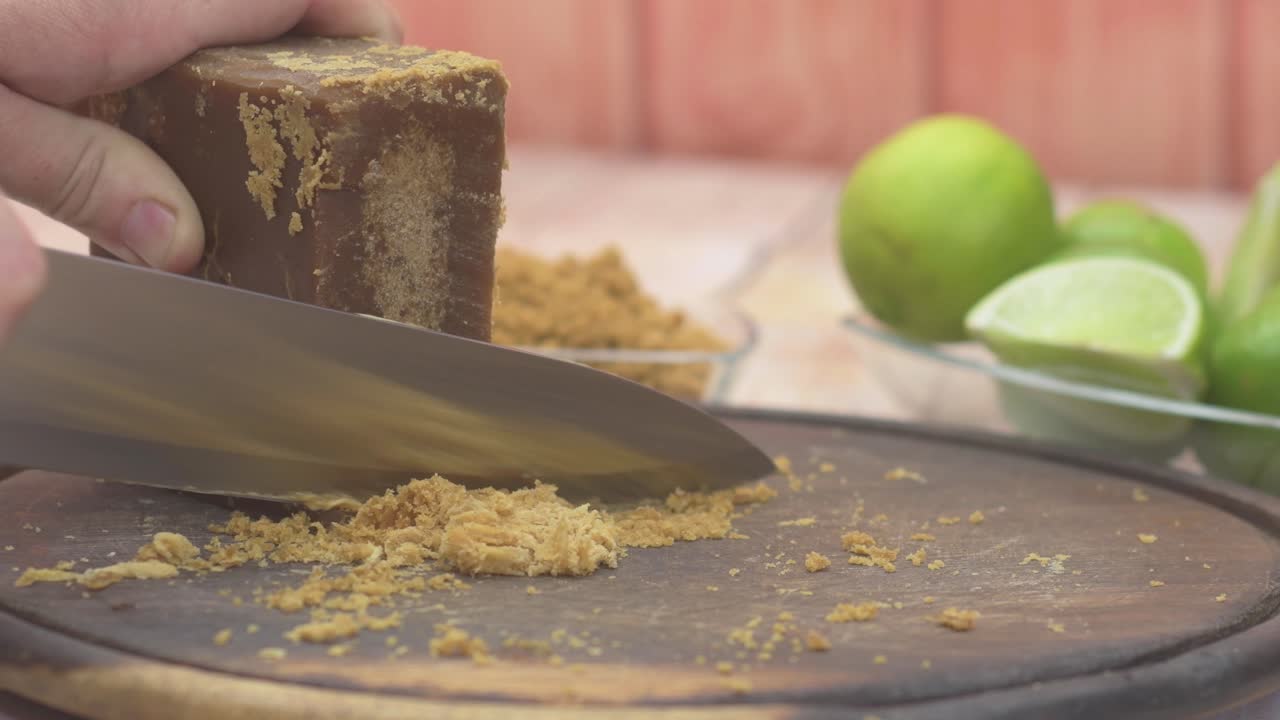 Preparazione di una ricetta tradizionale: una persona grattugia lo zucchero di canna su una tavola di legno con un coltello