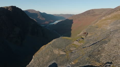 flying high over mountain walker stood on cliff edge at dawn over the honister pass with buttermere in the distance