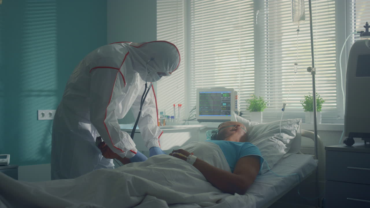 의사는 스테토스코프로 환자의 맥박을 듣고 있습니다. 병자는 의식을 잃고 누워 있습니다.