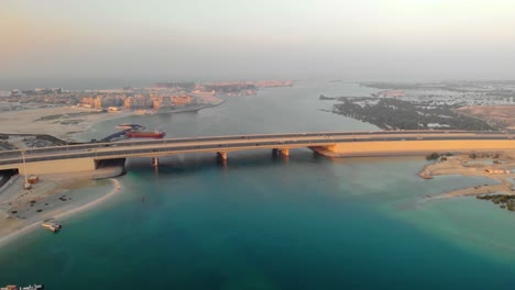 High-Altitude-drone-following-cars-drive-over-bridge-turquoise-water-Abu-Dhabi