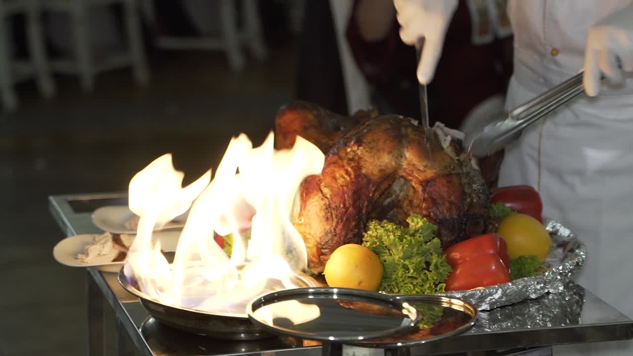 cook is cutting the baked chicken on the plate with vegetables near the fire on the summer terrace of the restaurant