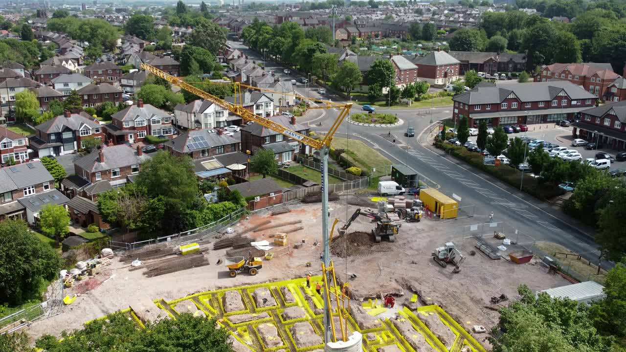 Rising above Tall crane setting building foundation in British town neighbourhood aerial view above suburban townhouse rooftops