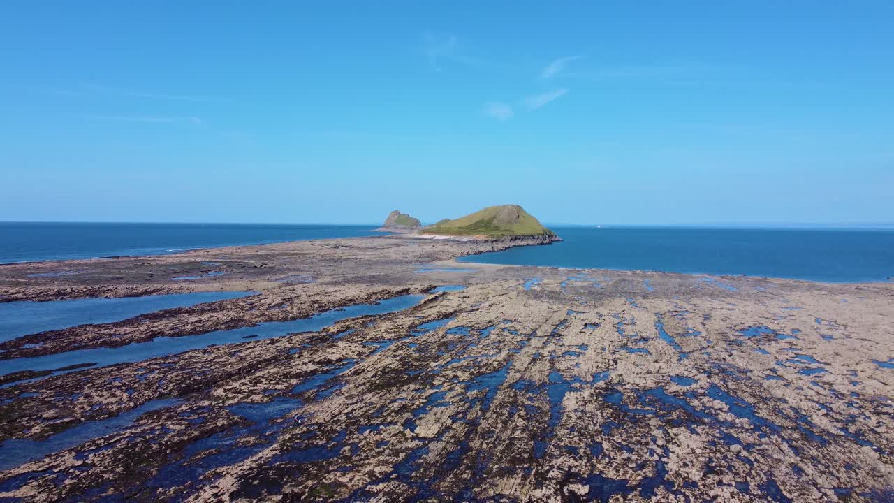 Descending Drone Shot of Worm's Head Landmark with Rocky Beach Coastline at Low Tide on Sunny Day in Summer. Filmed in Wales, UK.