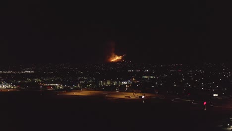 Human-caused-wildfire-breaks-out-in-the-foothills-above-a-sprawling-suburb-and-highway-at-night---aerial-view