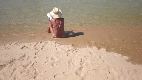 lady reads book while sitting at calm beach