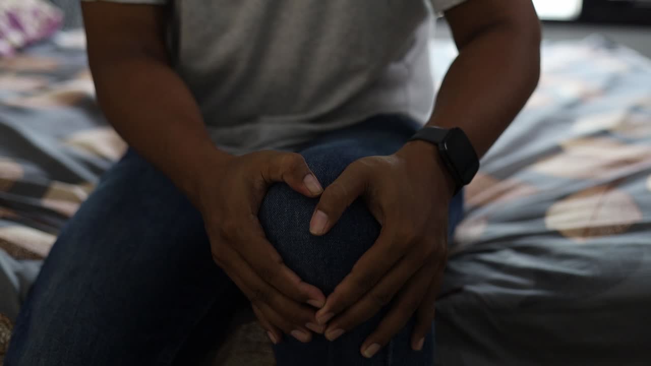 Closeup Asian man hand holding knee with pain on bed, health care and medical concept