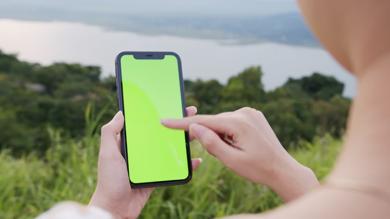 tiro de mano: mujer turista sosteniendo un teléfono de pantalla verde por la noche y una mujer usando una máscara para prevenir enfermedades.