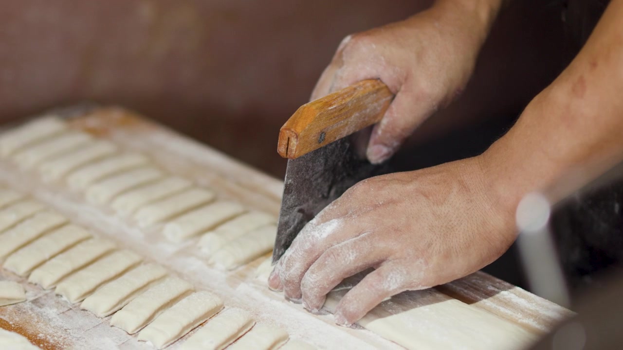 Close-up of hands cutting raw dough into uniform strips on a floured wooden surface.
