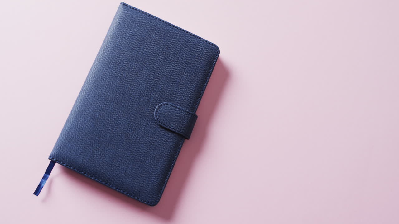 Close up of closed blue notebook with copy space on pink background in slow motion