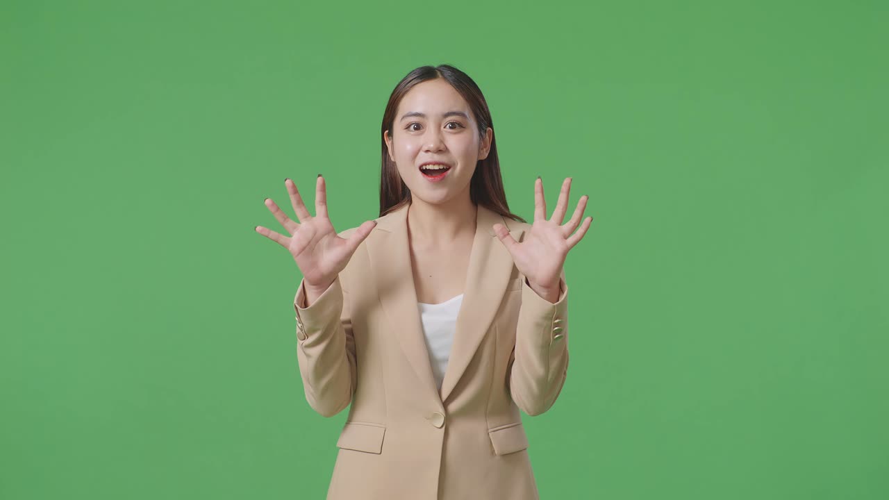 Una donna d'affari asiatica che mostra il palmo delle mani con un gesto di stupore dicendo "Wow" e sorride nello studio con schermo verde