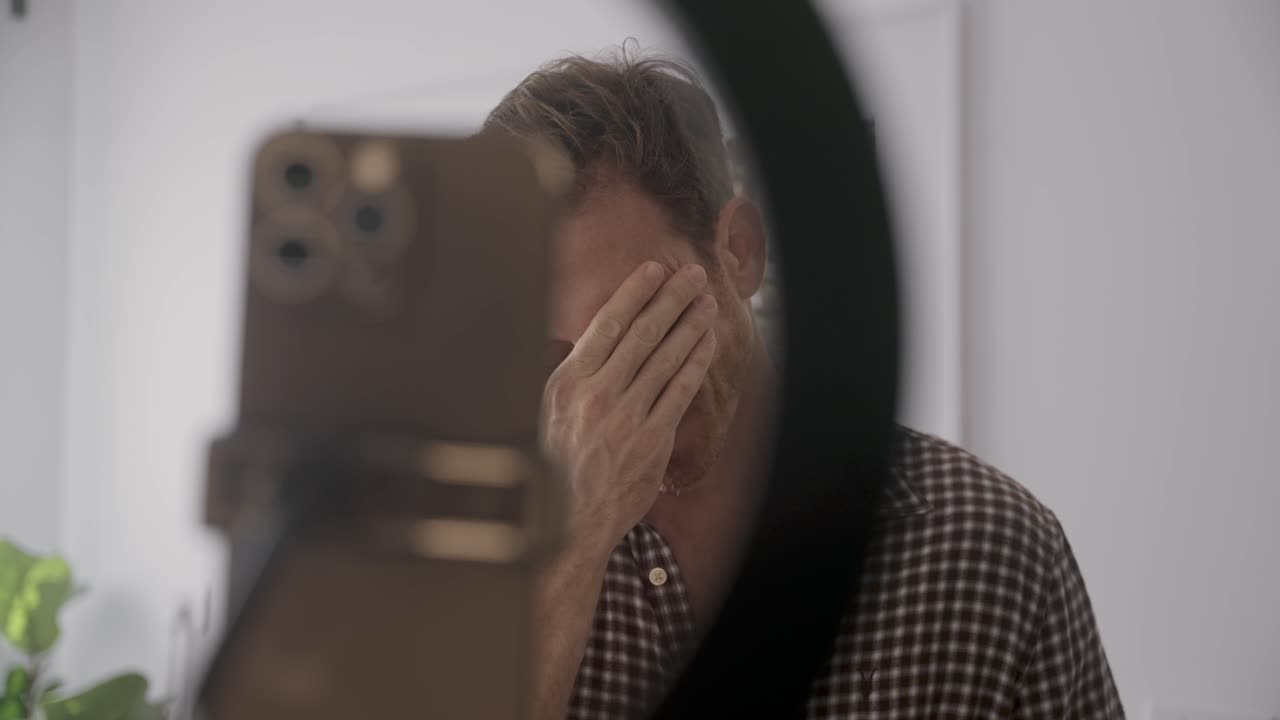 Criador de conteúdo gerado por usuários de redes sociais falando para a câmera do celular em um suporte com luz de anel em um apartamento ou casa. Triste e decepcionado, gravando um vídeo em modo selfie para o canal e fãs ou vlog pessoal