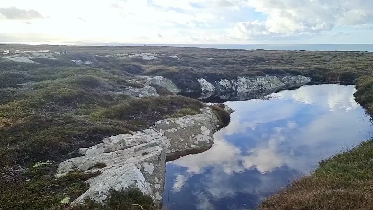 Rugged rocky welsh heather moorland panning to pool of water reflecting clouds