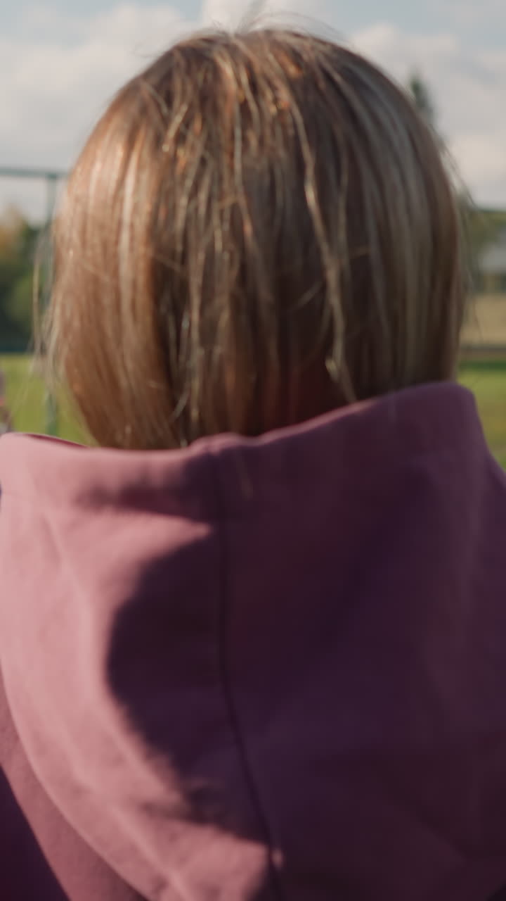 배경에는 바 울타리와 초록색으로 열린 코트에서 볼리볼을 연습하는 후디를 입은 여자의 뒷면, 이 많은 야외 스포츠 환경에서 개별 연습 기술에 초점을 맞추십시오.