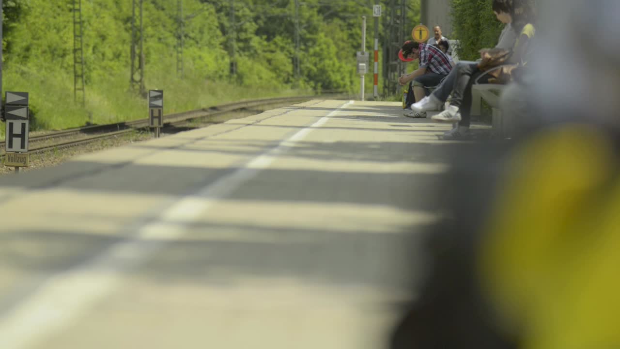 People waiting at a train station on a sunny day with lush greenery in the background