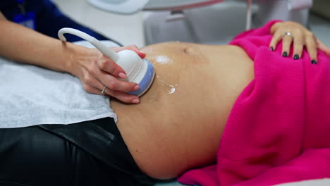 pregnant belly of a woman on the early stages of pregnancy. doctor's hand uses device to check the baby on the ultrasound machine.