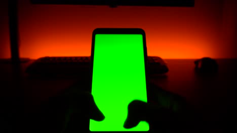 green screen: two thumbs typing on cellular phone in dark room with orange background light