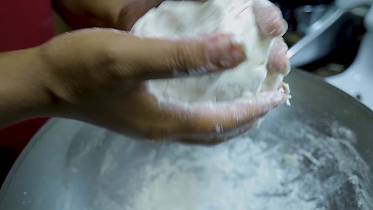 close up view of African american woman's hands kneading pizza dough in a silver pan in slow motion