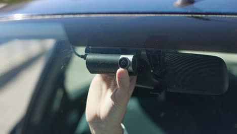 A-hand-adjusts-the-camera-of-a-dash-cam-attached-to-a-vehicle-windshield