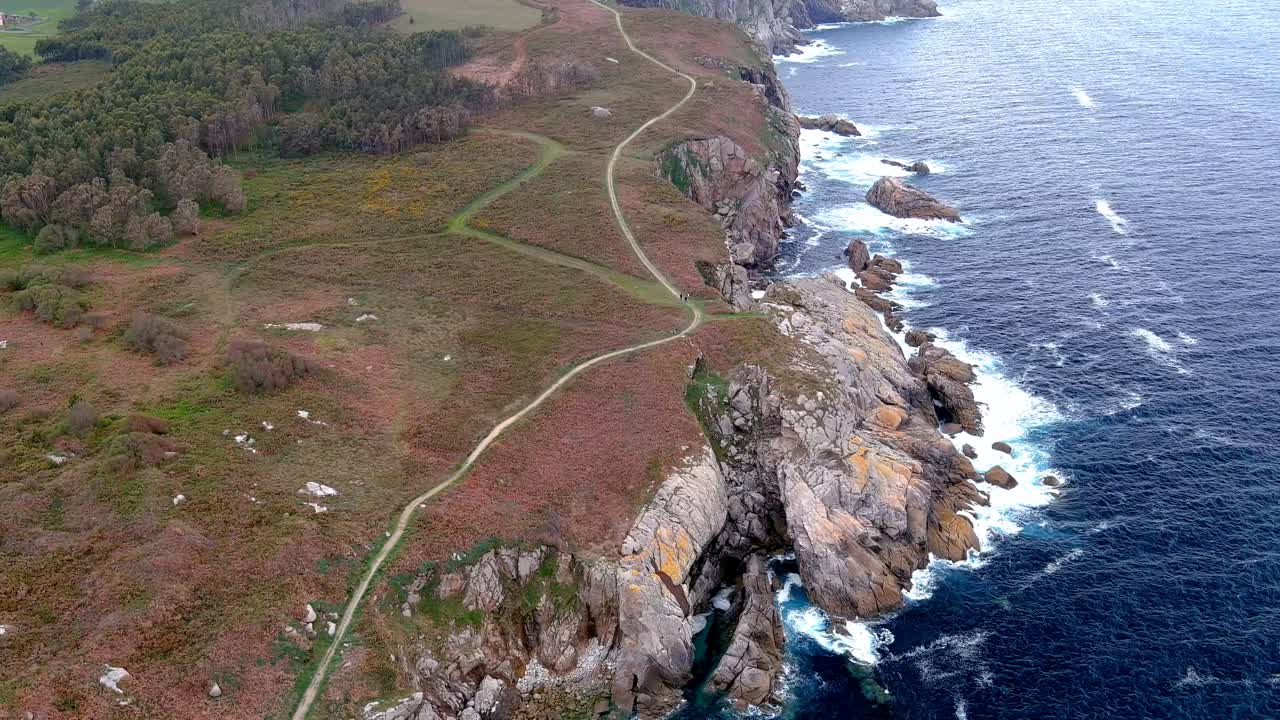 toma aérea de un camino estrecho a lo largo de acantilados escarpados, en la zona de morás, xove, lugo, galicia, españa con olas rompiendo a lo largo de la playa