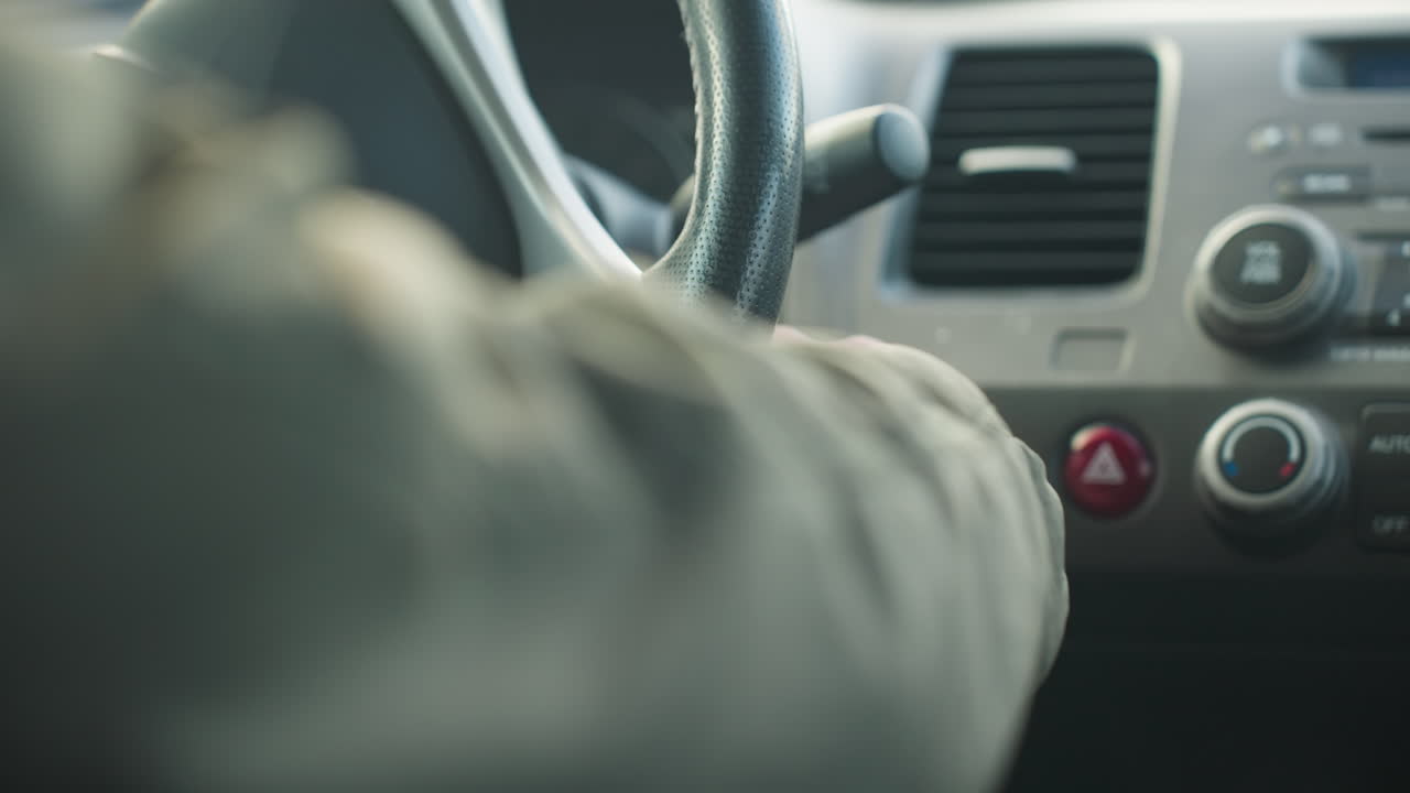 close up hand view of driver removing hand from ignition after turning on car, focus on steering wheel and dashboard area with climate controls and hazard button clearly visible