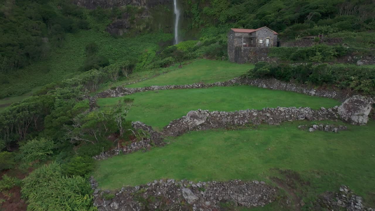 Reveal aerial shot of cascata do po&ccedil;o do bacalhau waterfall with house