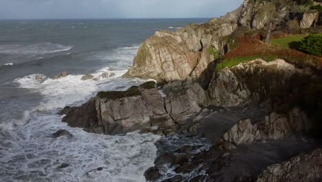 aerial drone orbit of a rocky cliff on the uk coastline with waves crashing into the cliff face - lee bay, beach, ilfracombe, devon, england