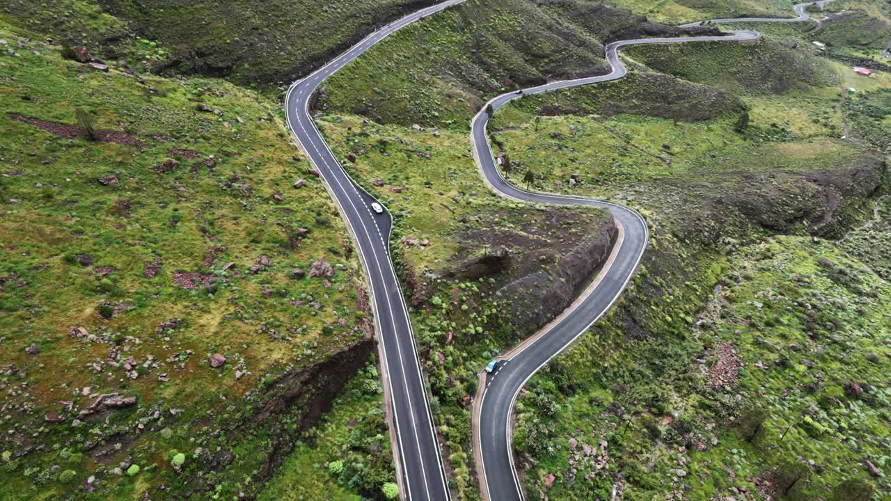 Perspectiva aérea de coches circulando por una carretera sinuosa a través de las verdes montañas de Los Azulejos de Veneguera en Mogán, Gran Canaria.